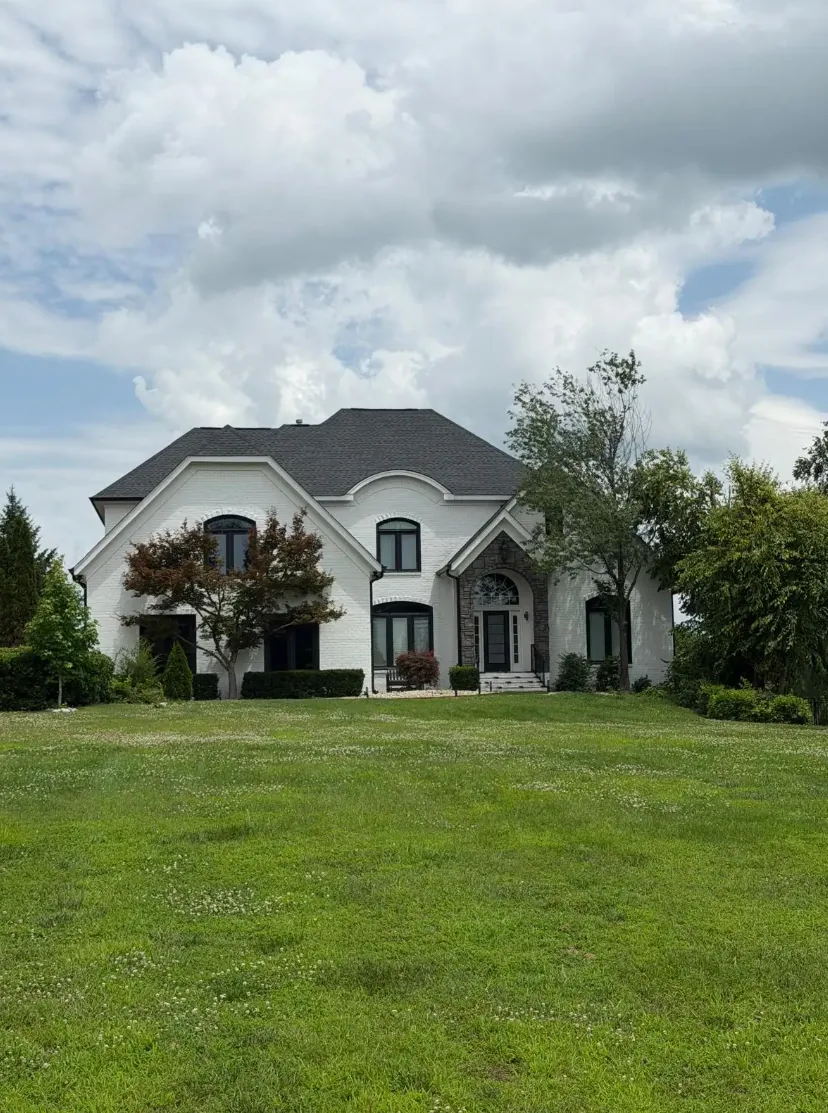 Large white brick home with a dark roof and landscaped front lawn